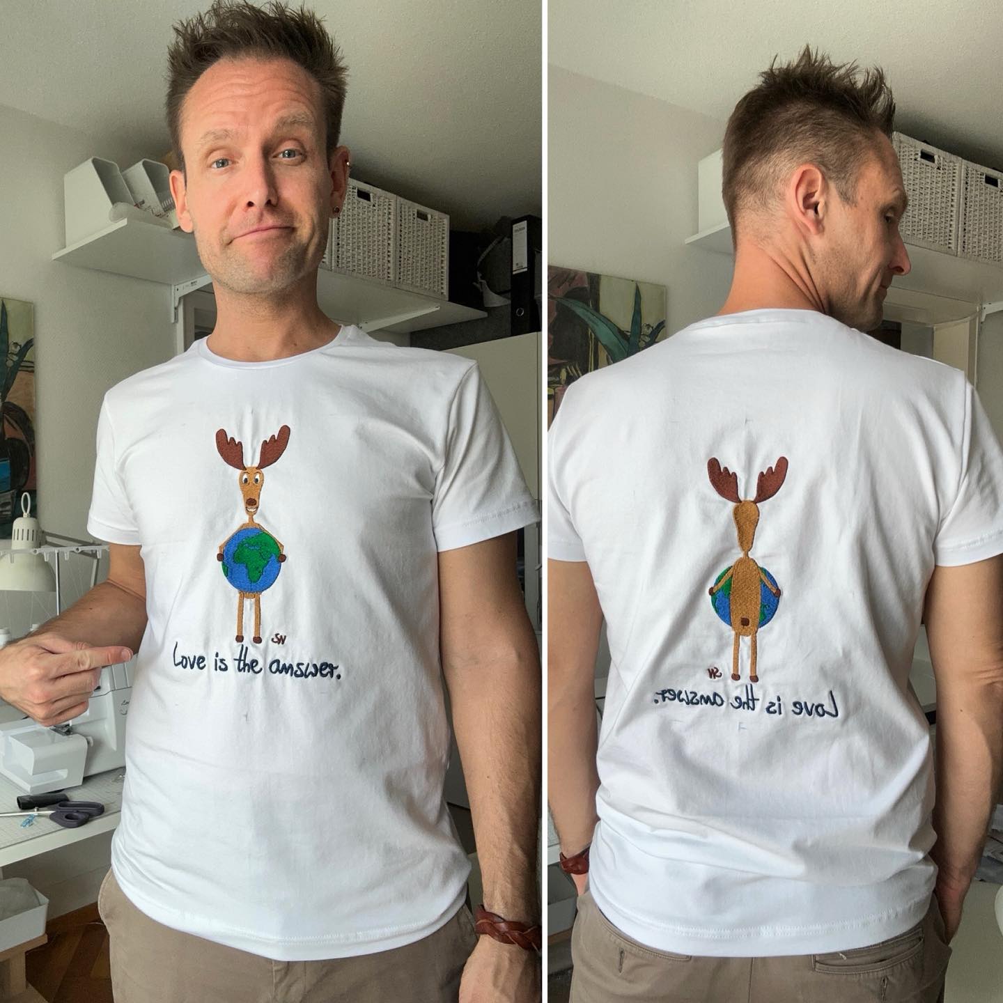 Sebastian Niklaus in seiner Nähwerkstatt. Er zeigt ein selbst genähtes T Shirt. Das Shirt ist weiß und darauf ist eine Stickerei. Sein Comic artiger Elch steht und hält eine Weltkugel u.a. mit Europa und Afrika. Darunter ist der Schriftzug